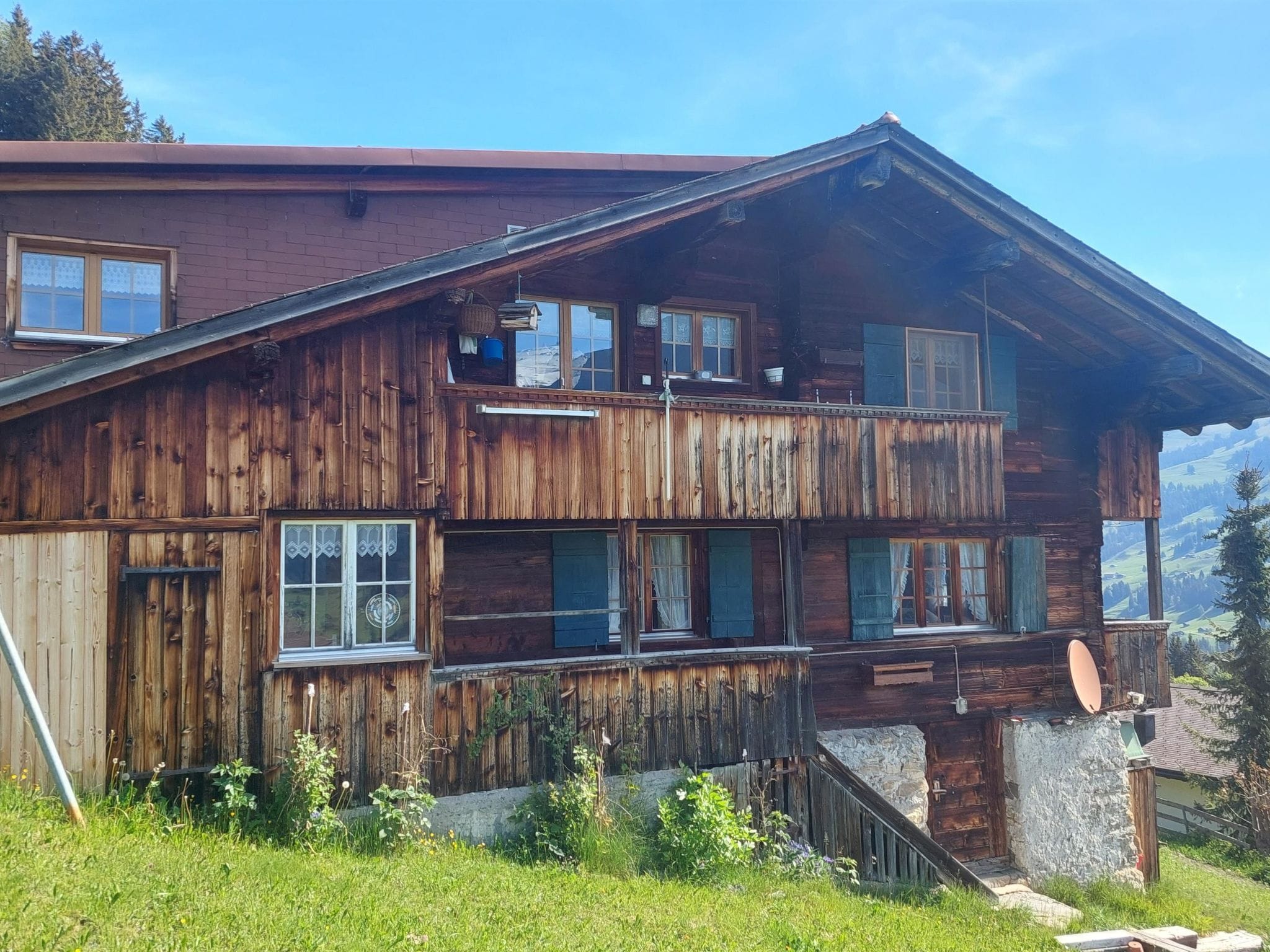 A wooden chalet with a balcony, multiple windows, and a stone foundation.