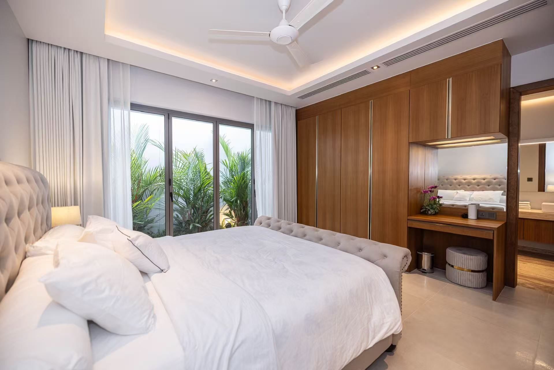 Habitación de hotel moderna con una cama grande, un tocador con espejo y vistas a zonas verdes.