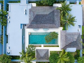 A modern resort with a central swimming pool, surrounded by palm trees and a blue building facade.