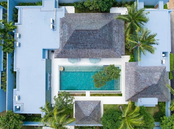A modern resort with a central swimming pool, surrounded by palm trees and a blue building facade.