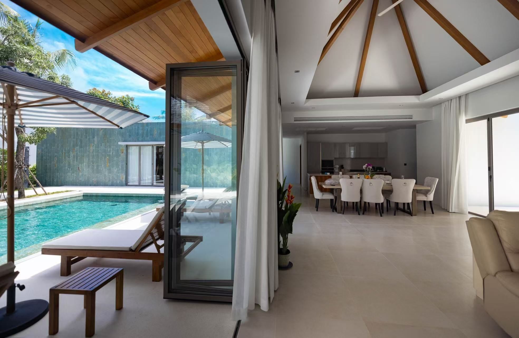 A modern interior with a dining area, kitchen, and a poolside lounge.