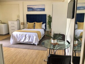 Et hotelværelse med seng, natbord, lampe og et stort spejl.