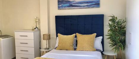 A bedroom with a bed, bedside tables, a lamp, a dresser, a potted plant, and a painting on the wall.