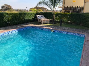 En swimmingpool med flisekant, omgivet af en murstenskant og en træterrasse.