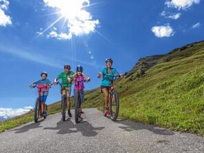 Vier fietsers op een verharde weg, met een heldere lucht en een heuvelachtig landschap op de achtergrond.