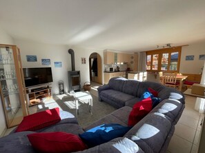A living room with a sofa, TV, and fireplace. There is a kitchen with wooden cabinets and a dining area with a table and chairs. - Am Gilsbach 2 Appartement/Fewo, Dusche und Bad, WC, 2 Schlafräume by Interhome (Adelboden)