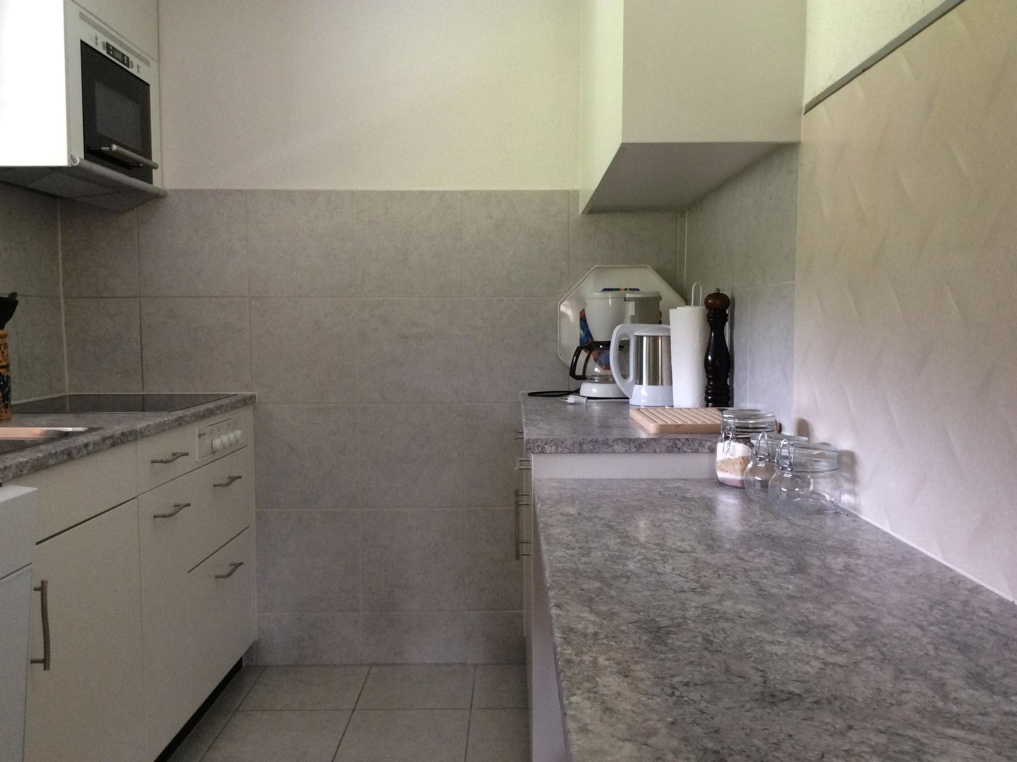 Uma cozinha com micro-ondas, cafeteira e jarra de café sobre o balcão.