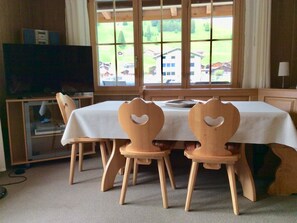 A dining area with a table and chairs, a television, and a window with a view of buildings and trees. - Bärgrose Appartement/Fewo, Bad, WC, 3 Schlafräume 4-Zimmerwohnung by Interhome (Adelboden)