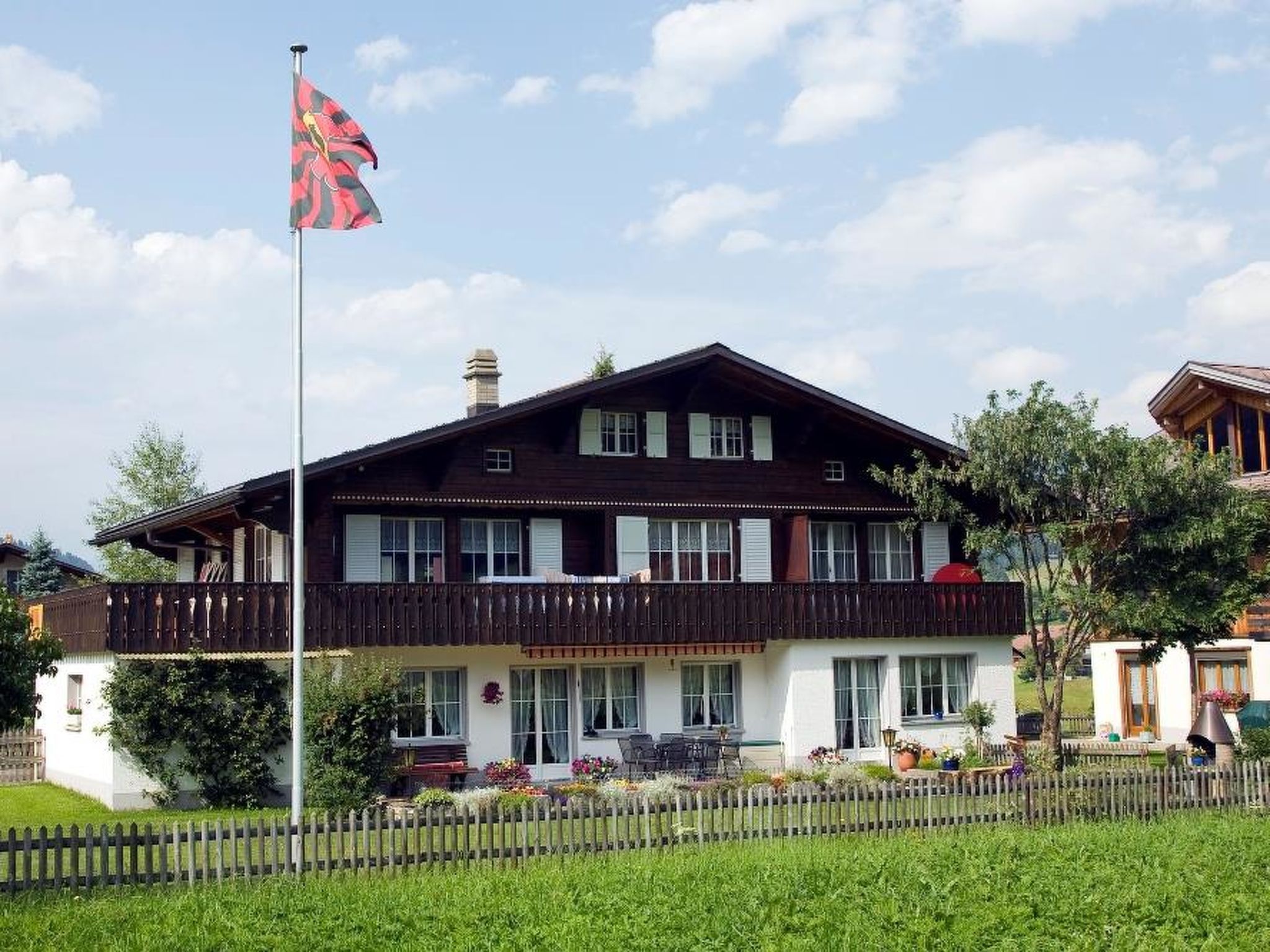 Ein zweistöckiges Gebäude mit einem Balkon, einer Fahnenstange mit einer Flagge und einem gepflegten Garten.