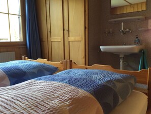 A room with two beds, a wooden wardrobe, a window with curtains, and a sink with a mirror above it. - Bärgrose Appartement/Fewo, Bad, WC, 3 Schlafräume 4-Zimmerwohnung by Interhome (Adelboden)