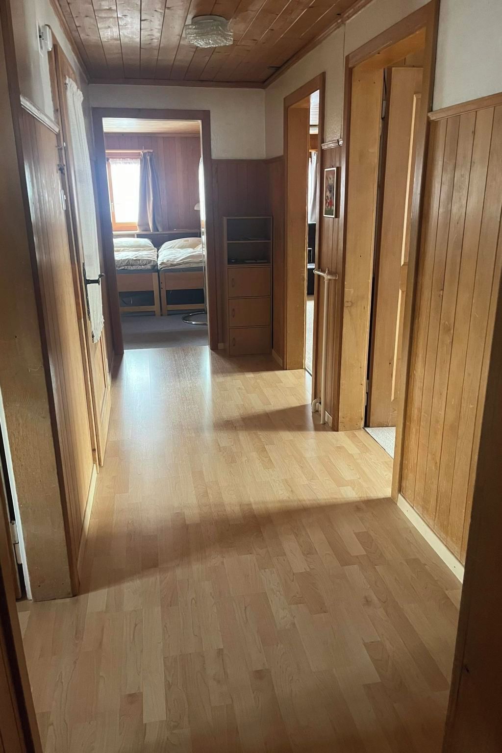 Un corridoio con pavimento in legno e porte che conducono a una camera da letto con un letto e un armadio.