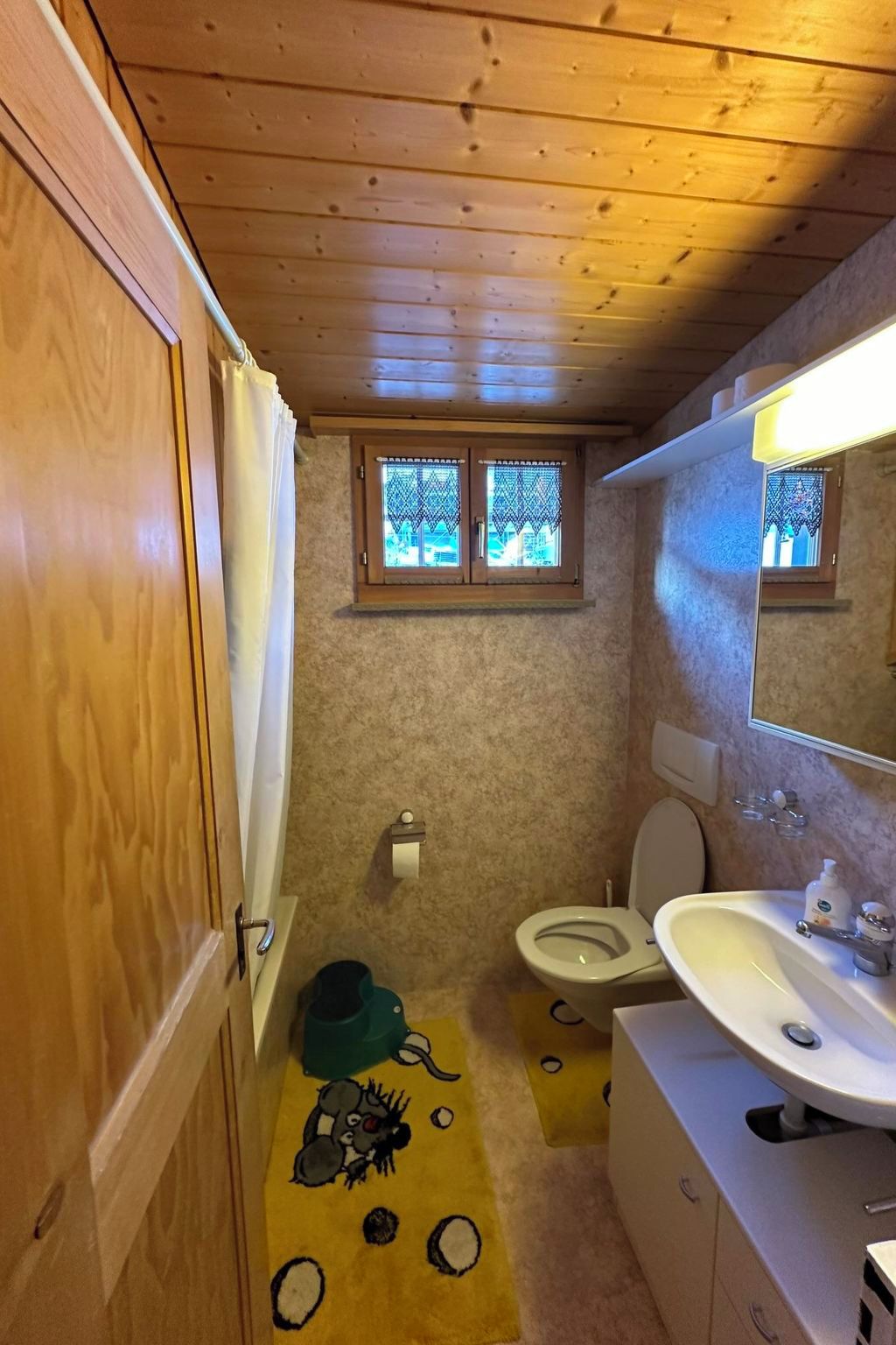 Une petite salle de bain avec des toilettes, un lavabo et une fenêtre agrémentée de rideaux à motifs.