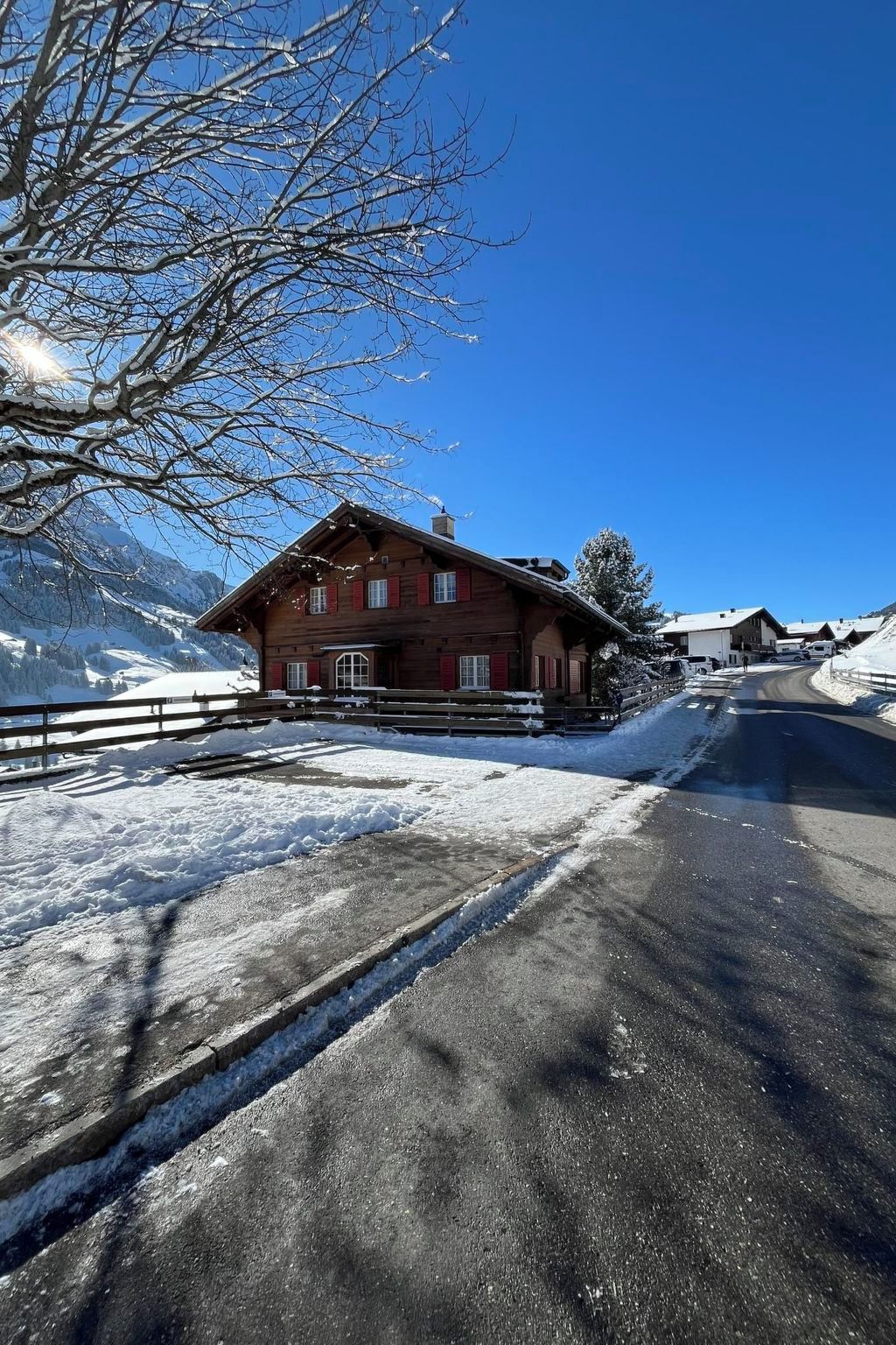 A wooden chalet with a sloped roof, a wooden fence, and a snow-covered landscape.