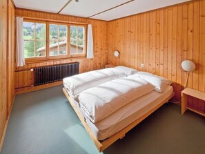 Ein Zimmer mit Holzwänden, einem Bett mit weißer Bettwäsche, einem Fenster mit Vorhängen und einem Heizkörper.