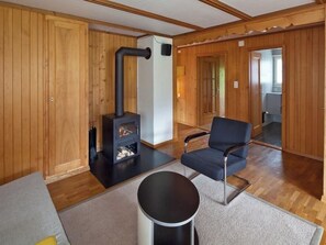Ein gemütliches Zimmer mit Holzwänden, einem schwarzen Kamin, einem blauen Sessel und einem kleinen runden Tisch.