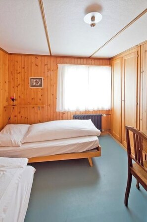 Ein Zimmer mit Holzwänden, einem Bett, einem Sessel und einem Fenster mit Vorhängen.