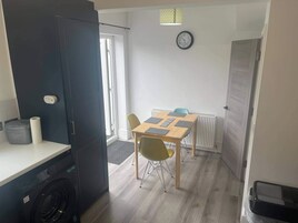 Cocina compacta con lavadora, comedor con mesa y sillas, y un reloj en la pared.