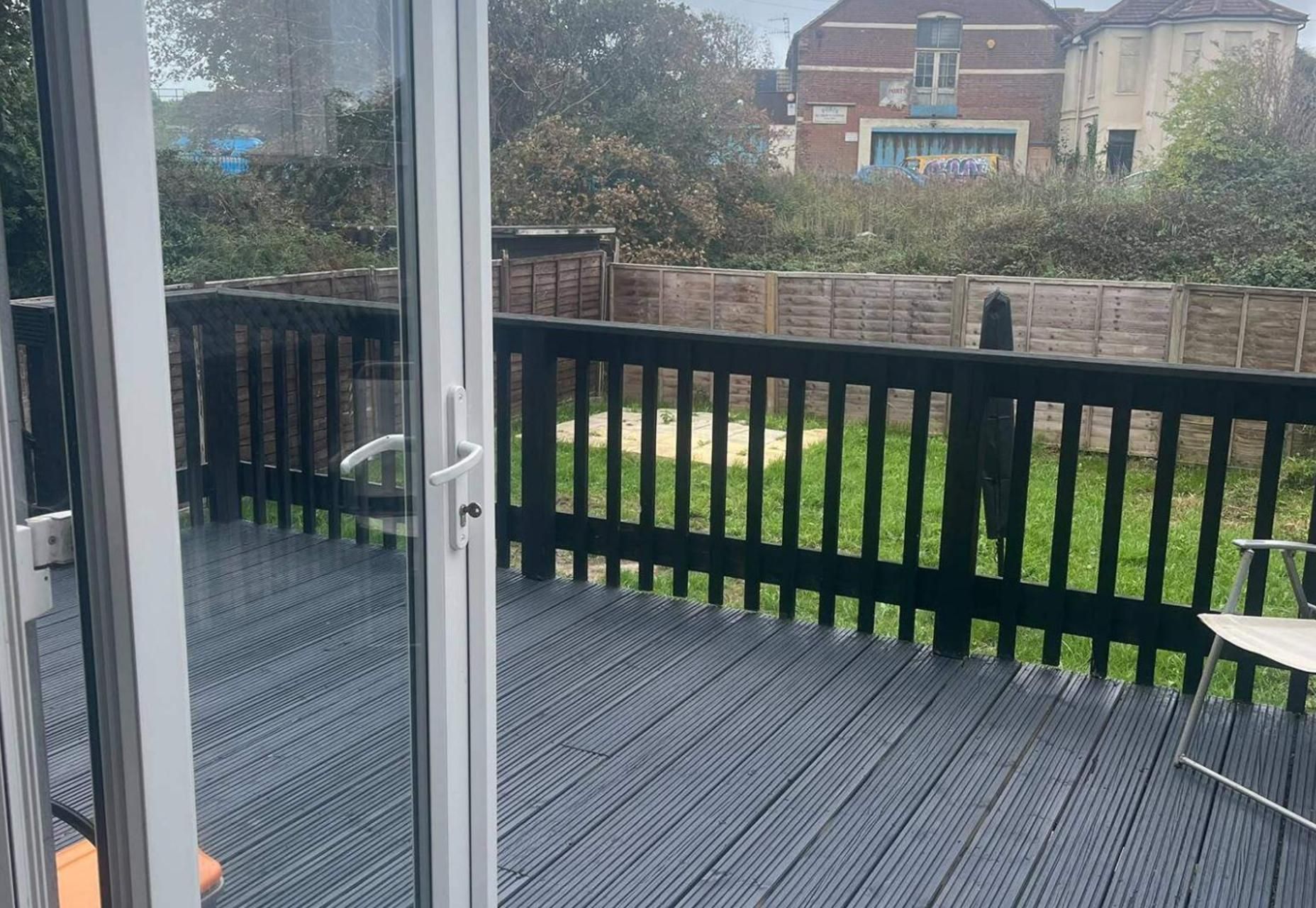 A deck with a glass door leading to a backyard with a wooden fence and a grassy area.