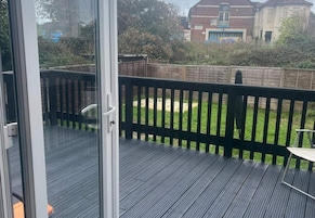 Una terraza con puerta de vidrio que da a un patio trasero con cerco de madera y zona verde.