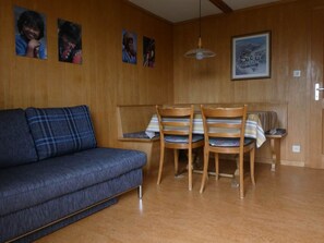 Ein Zimmer mit einem blauen Sofa, zwei Holzstühlen, einem Esstisch mit gestreiftem Tischläufer, Holzwänden und einem gerahmten Bild an der Wand.