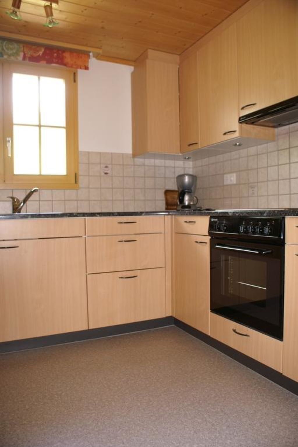 Une cuisine avec des meubles de rangement en bois, un poêle noir et une fenêtre avec un rideau.