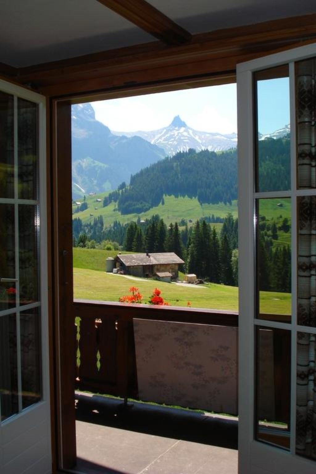 A room with a large window overlooking a mountainous landscape with a house and greenery.