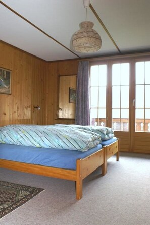 Ein Zimmer mit einem hölzernen Bett, einer Pendelleuchte und einem großen Fenster mit Vorhängen.