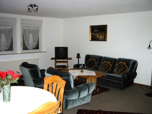A living room with a sofa, chairs, a television, a painting, and a window with curtains. - Chalet im Ahori Appartement/Fewo, Dusche oder Bad, WC 3-Zimmerwohnung by Interhome (Kandersteg)