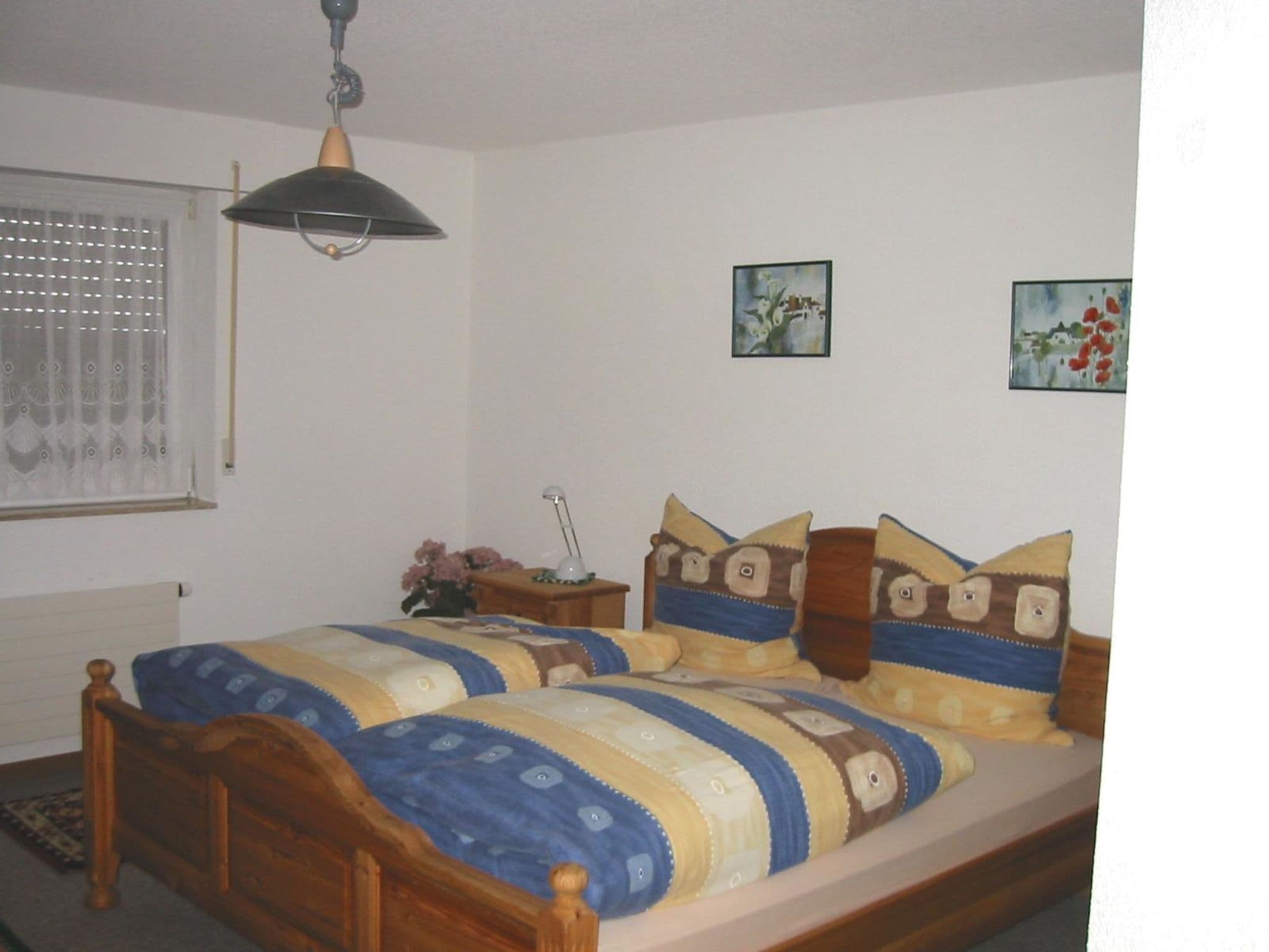 A bedroom with a wooden bed, a nightstand, a lamp, and two wall-mounted paintings.