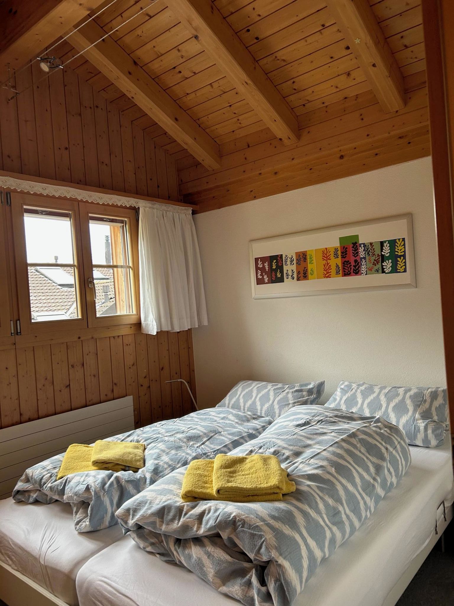 A room with wooden walls and ceiling, a bed with striped bedding, two pillows, and a framed artwork on the wall.