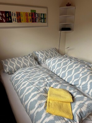 A bed with patterned bedding and a yellow towel. - Am Gilsbach Appartement/Fewo, Dusche und Bad, WC, 2 Schlafräume by Interhome (Adelboden)