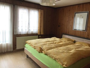 A bedroom with a bed, wooden walls, a radiator, and a window with curtains. - Sunnegruess Appartement/Fewo, Dusche, WC, 2 Schlafräume 3-Zimmerwohnung by Interhome (Adelboden)