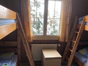 Ein Schlafsaalzimmer mit Etagenbetten, einem kleinen Holztisch und einem Fenster mit Blick auf Bäume.