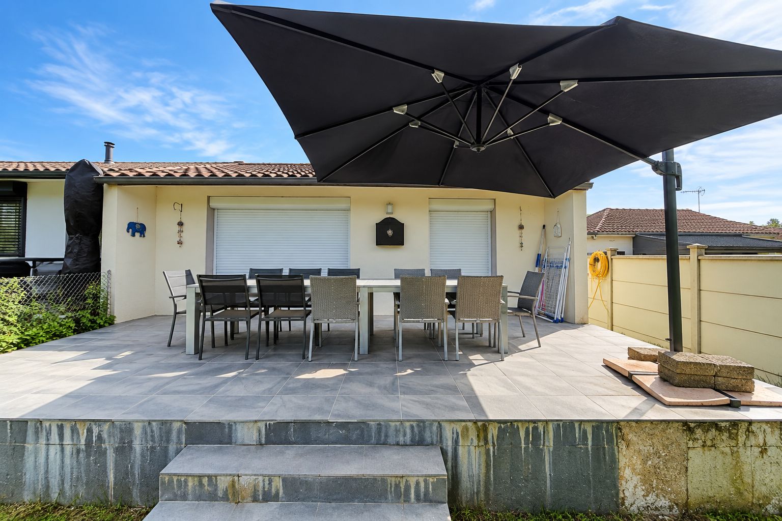 Eine Terrasse im Freien mit Tisch und Stühlen, einem großen Sonnenschirm und einer Garagentür.