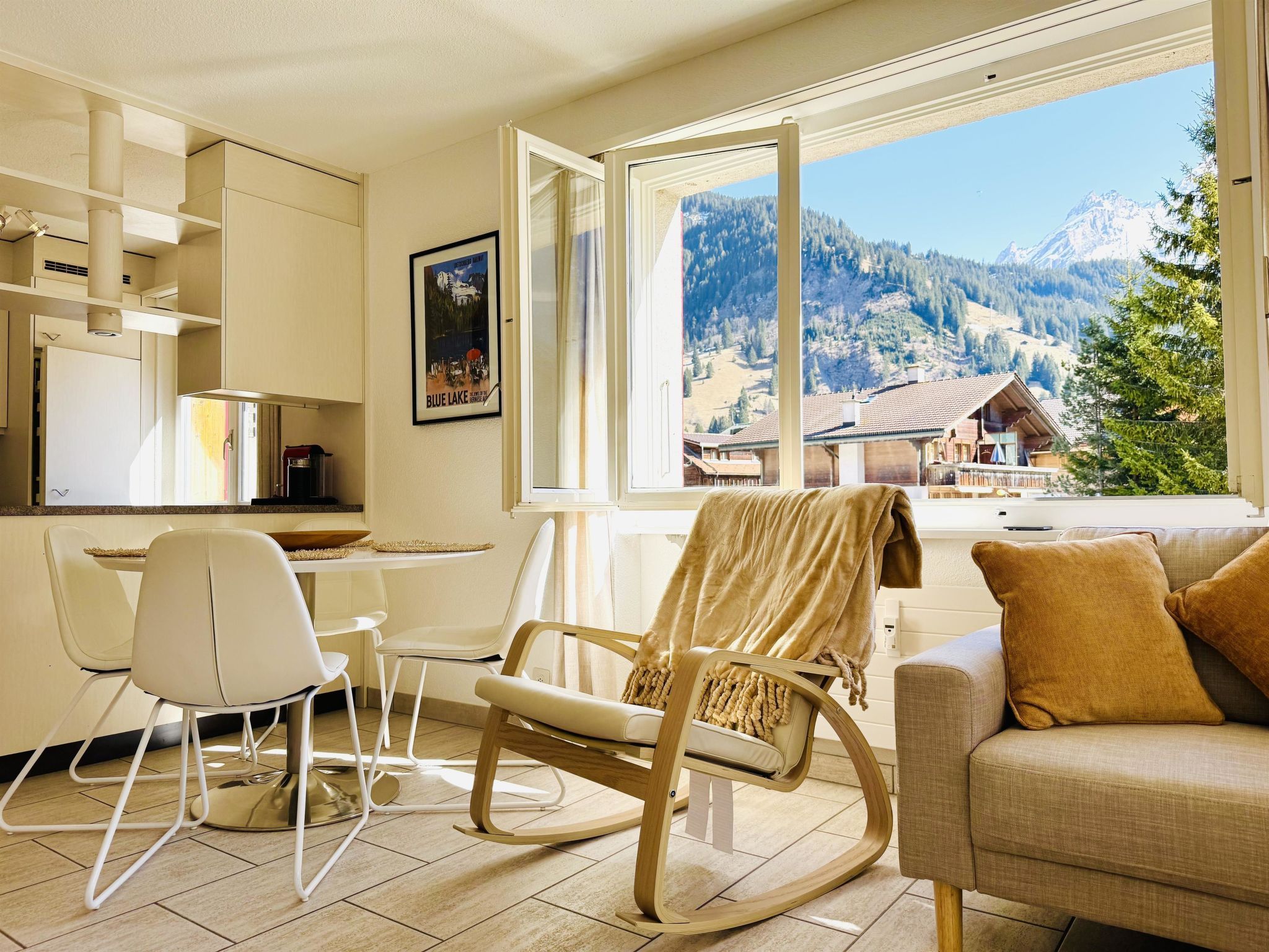 Een moderne woonkamer met uitzicht op een berglandschap, een eethoek met een tafel en stoelen, en een keuken met kasten en een raam.