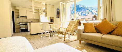A hotel room with a bed, a sofa, a chair, a desk, and a view of a mountainous landscape.