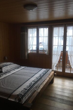 A room with a large bed, wooden flooring, and a sliding glass door leading to an outdoor area. - Elim Appartement/Fewo, Bad, WC, 4 oder mehr Schlafräume 5.5 Zimmerwohnung by Interhome (Adelboden)