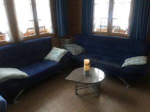 Una habitación con dos sofás azules, una mesita redonda con una vela y una ventana con cortinas.