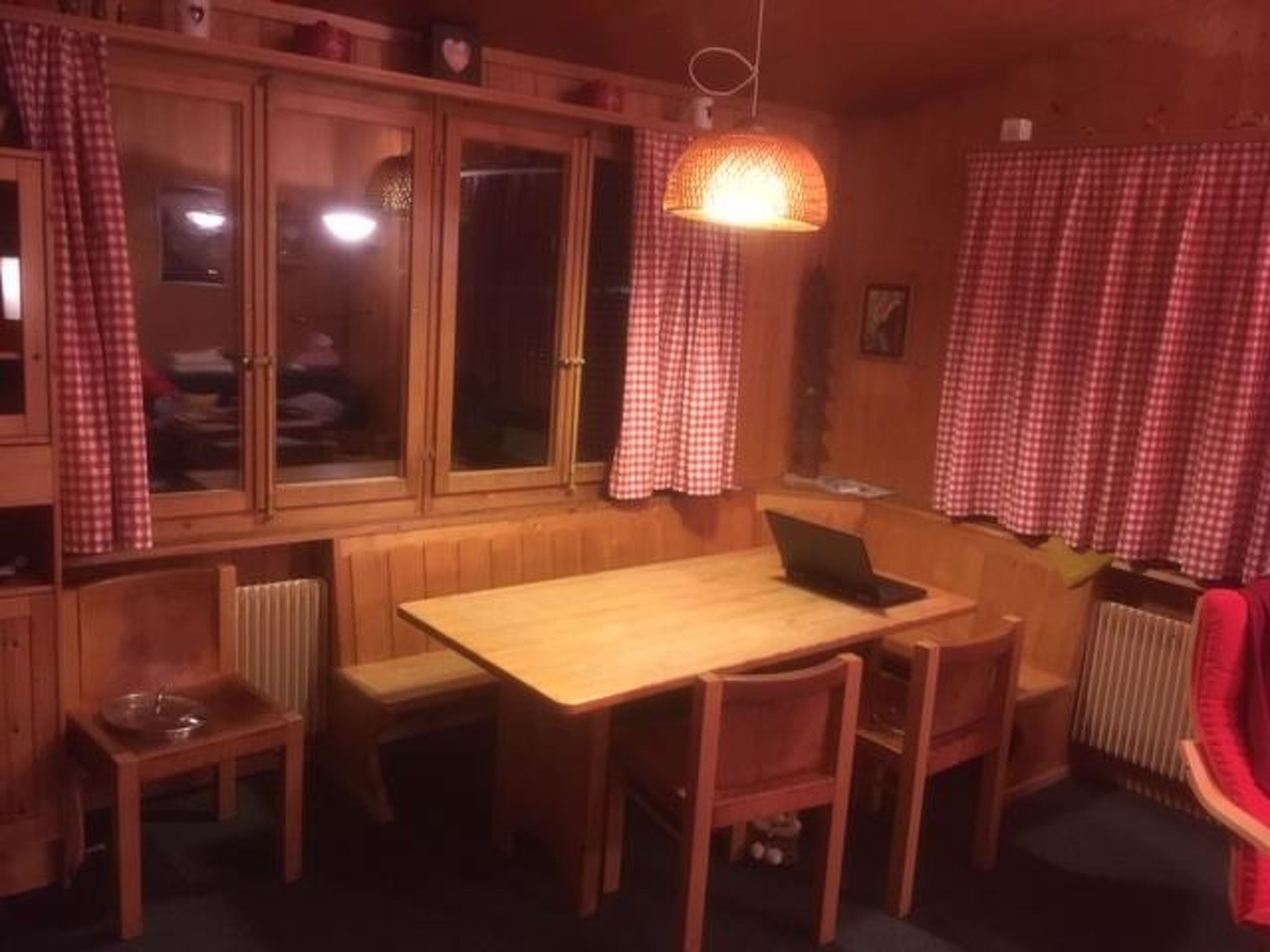 Una habitación acogedora con una mesa y sillas de madera, un banco, un radiador y cortinas a cuadros.
