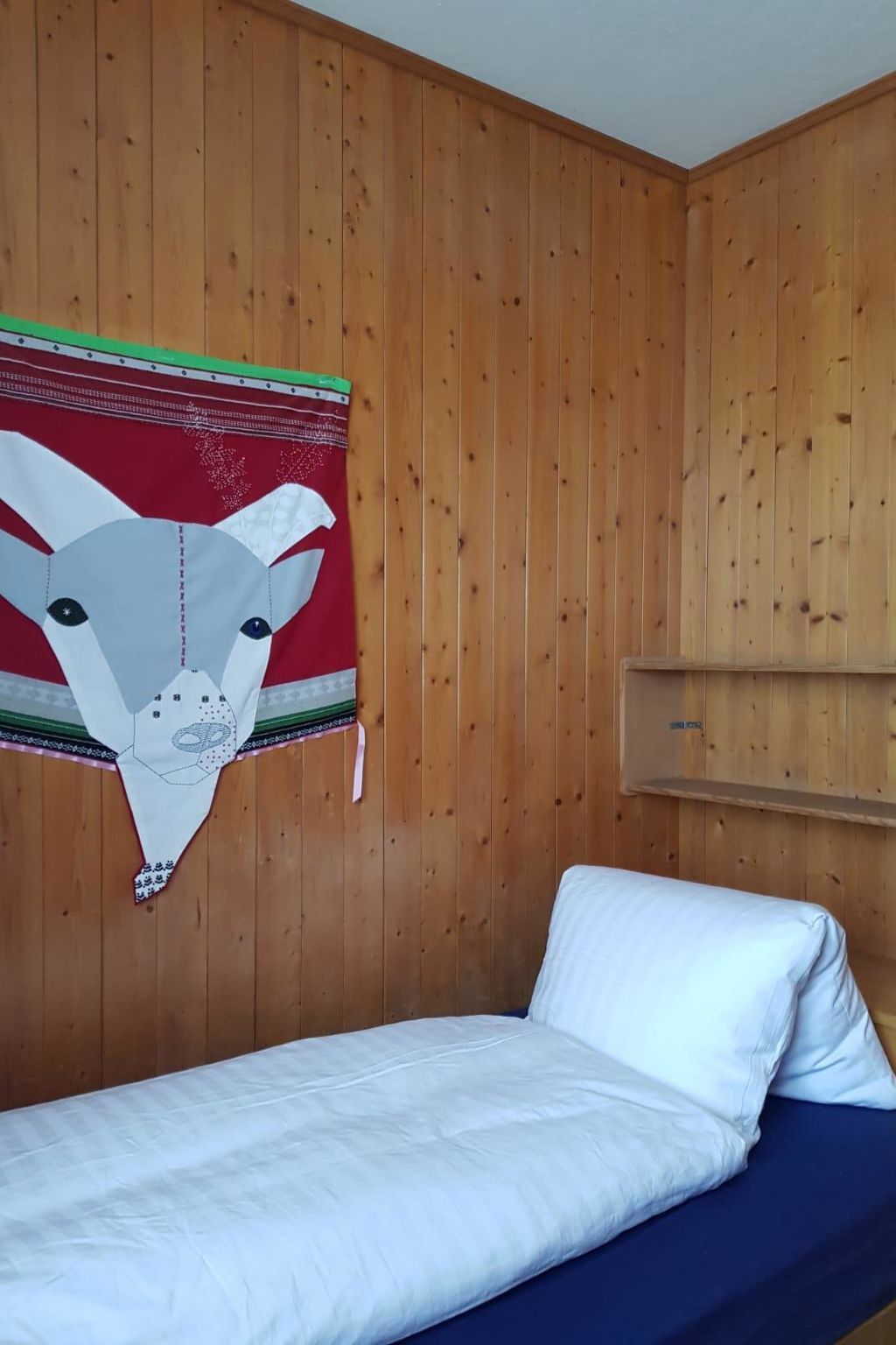 A room with wooden panel walls, a bed with white and blue bedding, and a wall hanging of a cow's head.