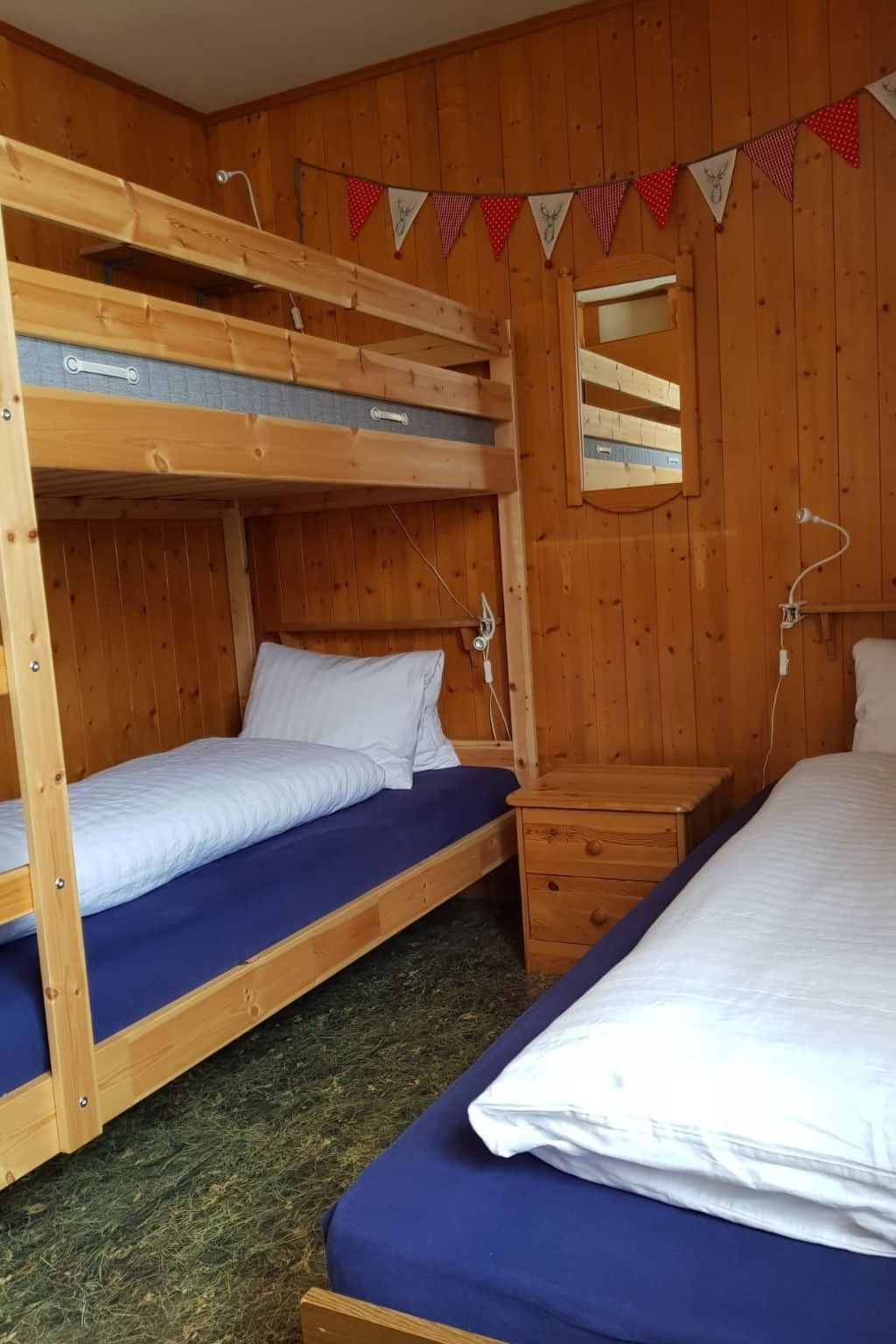 Ein Schlafraum mit Etagenbetten, Holzwänden, einem Spiegel und einer Girlande aus roten und weißen dreieckigen Flaggen.