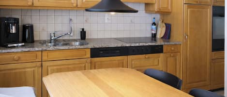 Una cocina con armarios de madera, una lámpara colgante negra, una cafetera y una botella de vino.