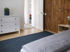 Une chambre à coucher avec un lit, une commode, une table de chevet, une lampe et un mur en bois.
