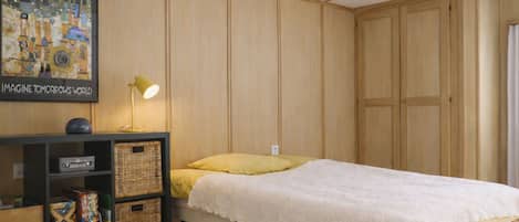 Une chambre à coucher avec un lit simple, une table de chevet, une lampe, une bibliothèque et un tableau encadré au mur.