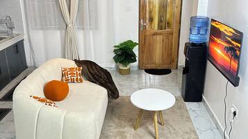 A compact living space with a sofa, a small table, a water dispenser, a TV, and a door with a window.