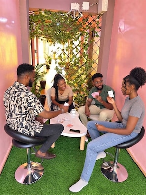 Un grup de persones assegudes al voltant d'una taula en una habitació amb terra de gespa artificial i una paret decorativa de plantes.