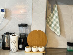 Una cocina con hervidor, licuadora, tabla de cortar de madera y un paño colgado en la pared.