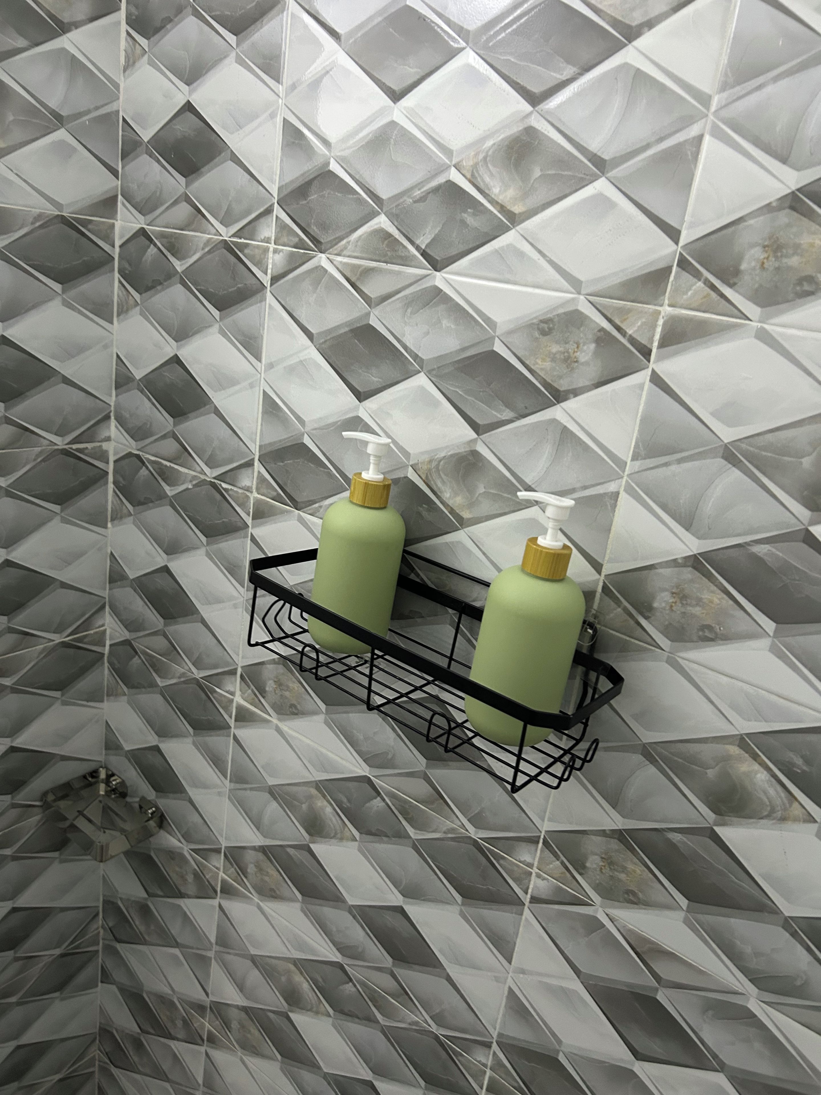 A bathroom with a geometric patterned tile floor and a black metal rack holding two bottles.