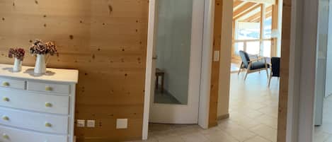 A wooden interior with a white dresser, a door leading to a balcony, and a view of the outdoors.