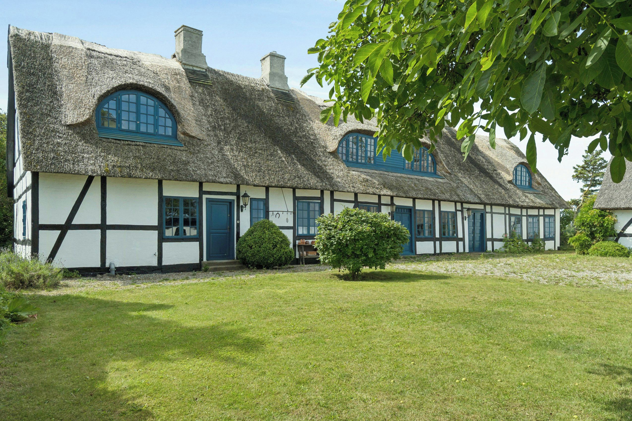 A traditional thatched-roof house with a white exterior and blue accents, surrounded by a well-maintained lawn.